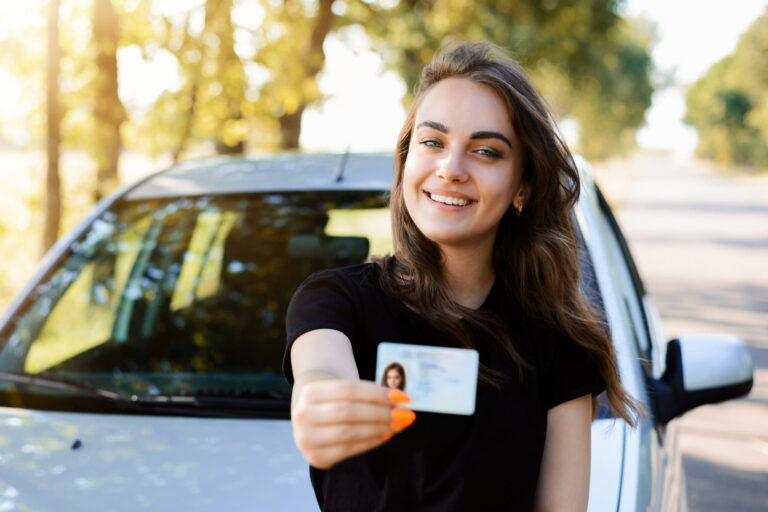 pretty girl with cheerful smile standing near car showing driving license front woman expresses her happiness after passing driving exam 1 768x512